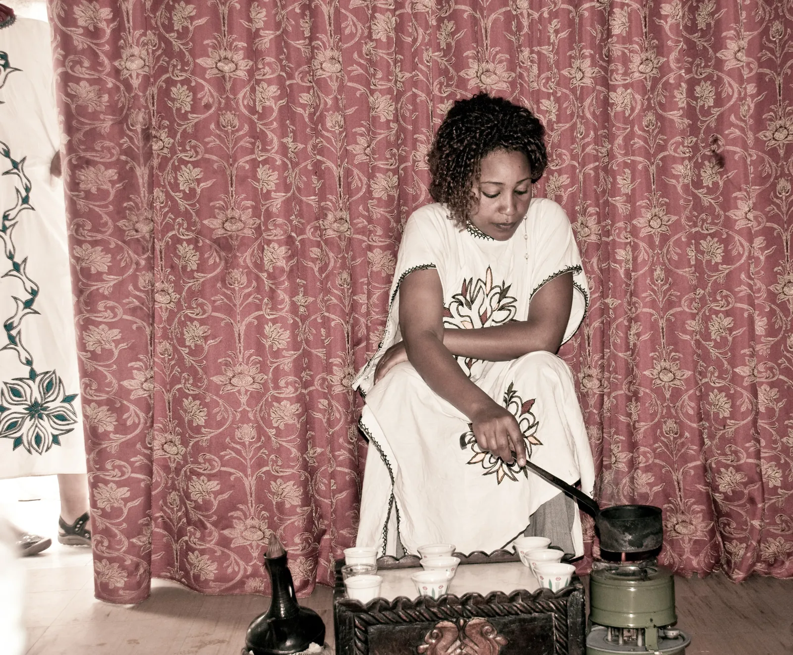 A woman preparing coffee with a clay jebena and small cups