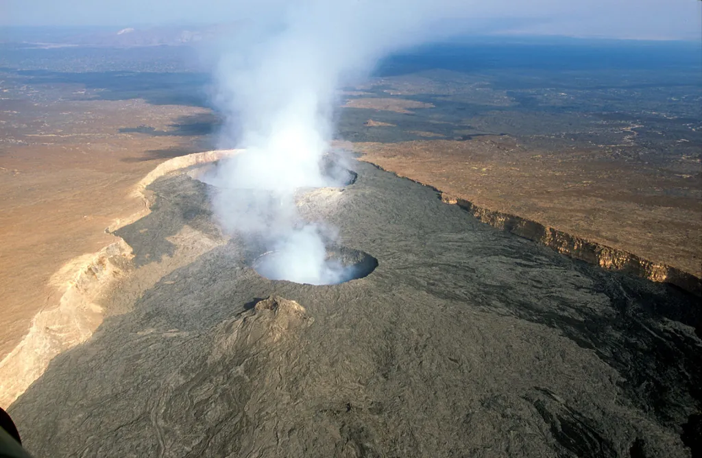 A plume rising from the crater of Erta Ale above a dark volcanic landscape